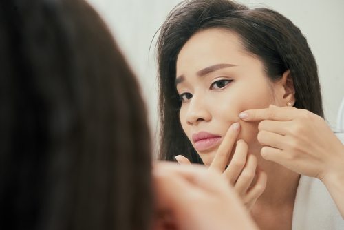Young woman popping a pimple on her cheek