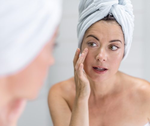 middle aged woman looking at eye wrinkles in mirror