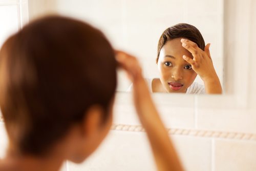 woman looking in mirror, covering area on forehead